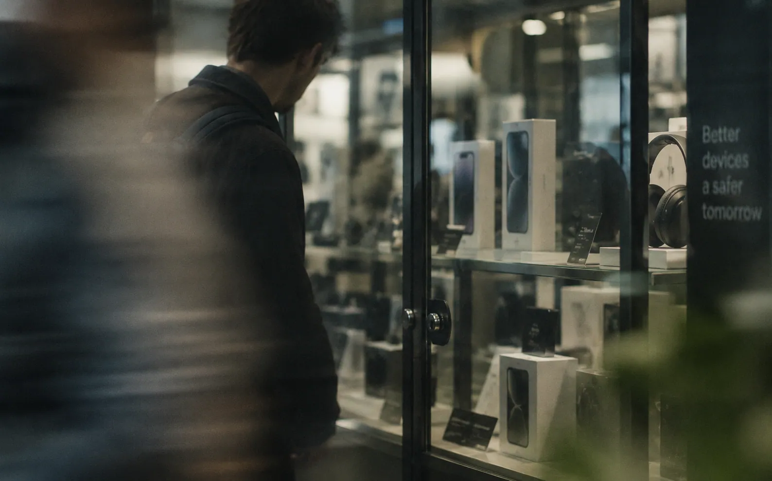 A shopper waiting at a locked electronics cabinet of phones and headphones